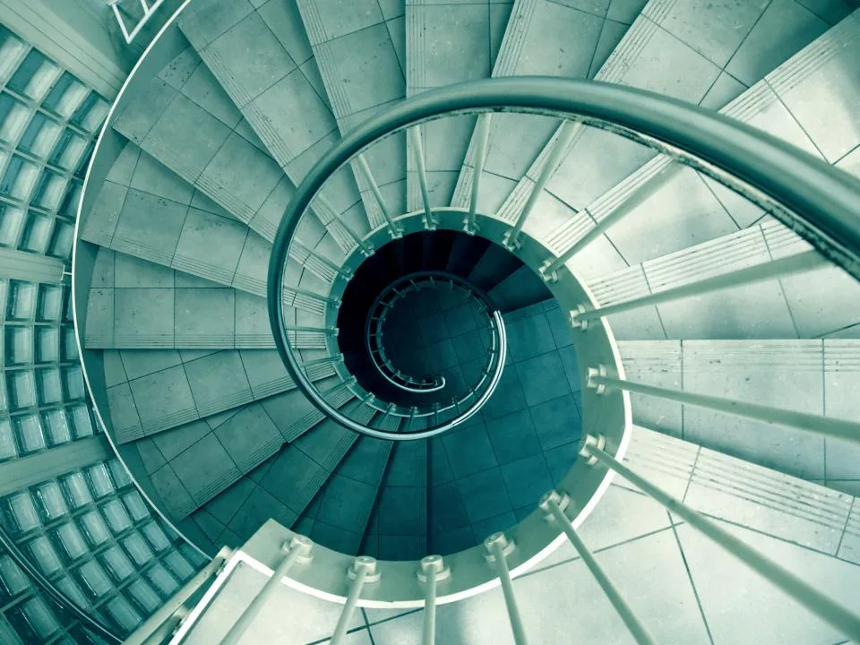 Looking down a spiral concrete staircase with a curved metal handrail