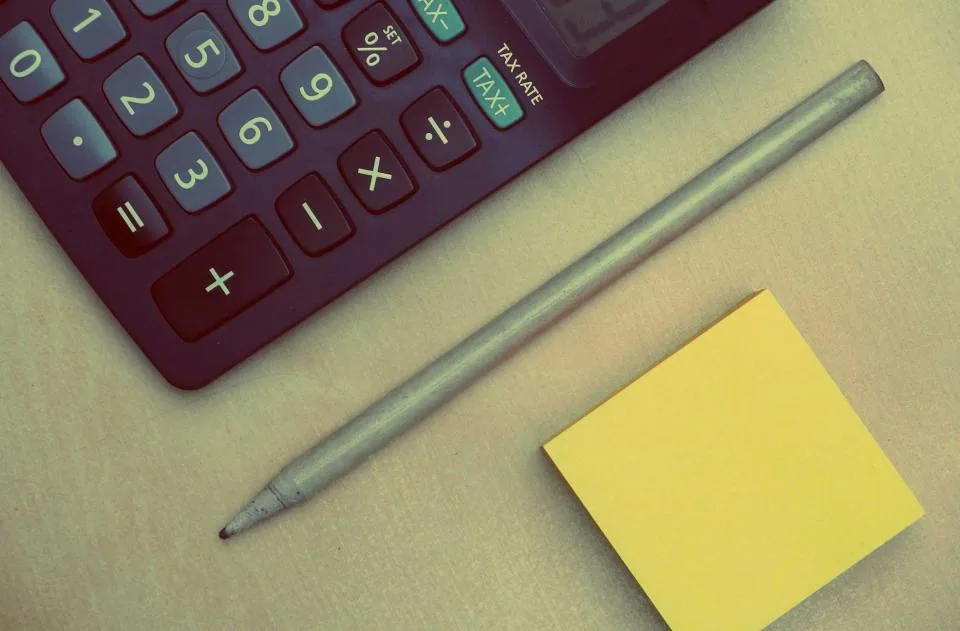 Calculator, pencil and a yellow sticky note on a desk