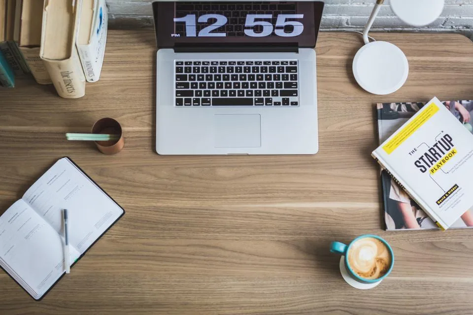 A tidy desk with a laptop, notebook and coffee