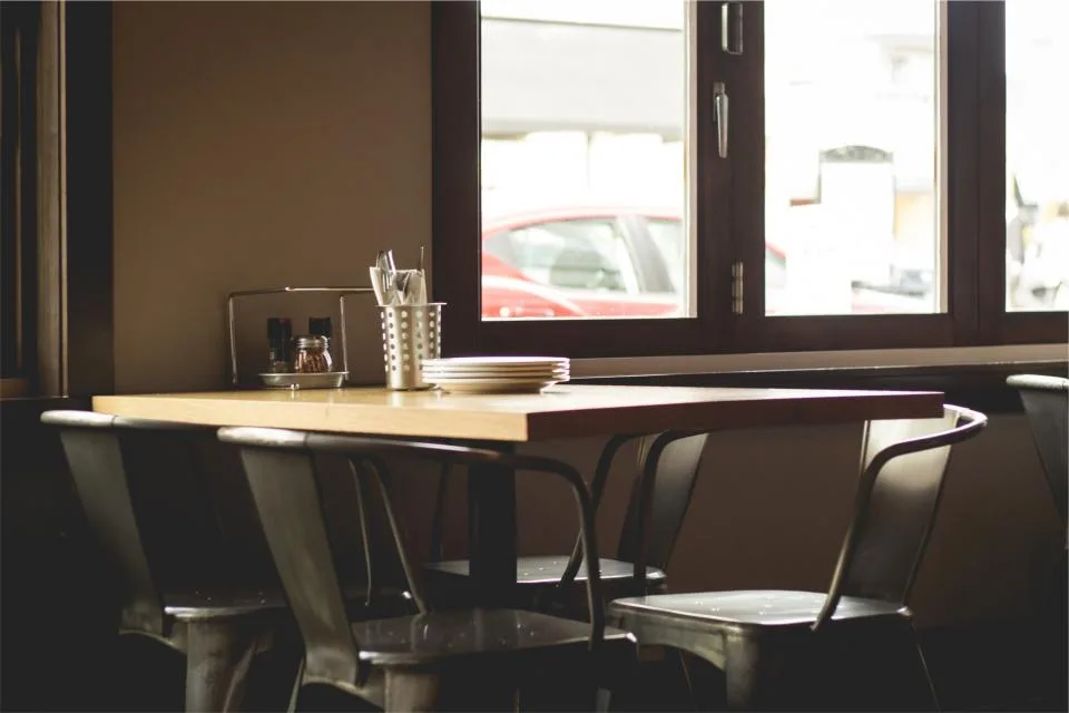 Empty cafe table and metal chairs beside a window in soft evening light
