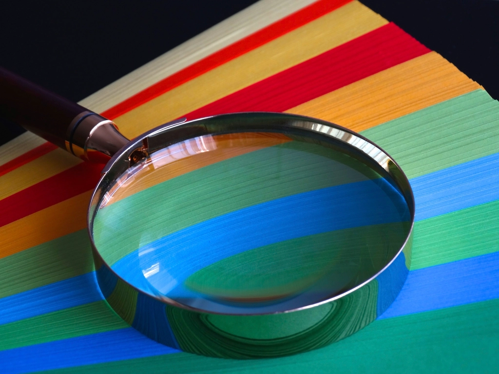 A magnifying glass resting on a stack of colorful paper