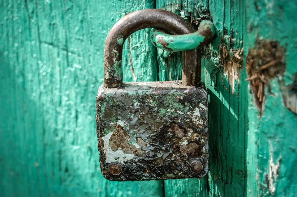 An old, rusty padlock hanging on a weathered green wooden door