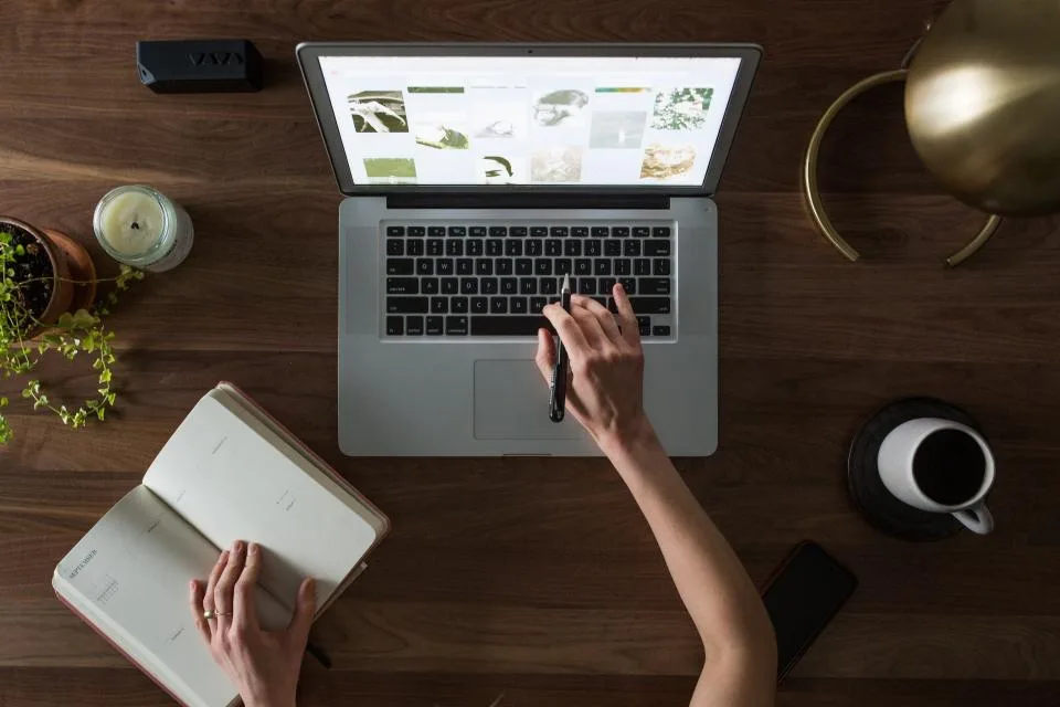 Person working at a laptop with a notebook and coffee