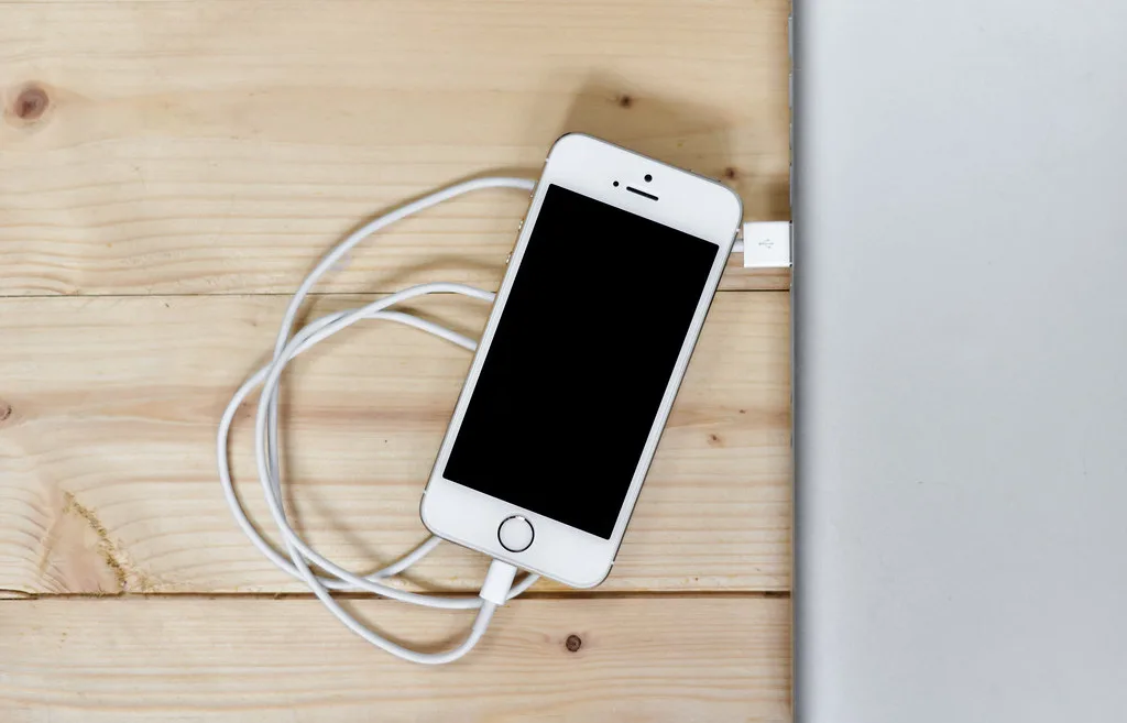 A smartphone with a charging cable lying on a wooden desk