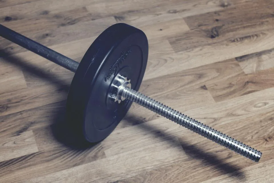 A barbell with black weight plates resting on a wooden gym floor