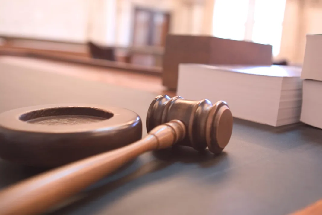 A wooden gavel on a courtroom bench beside stacks of paper