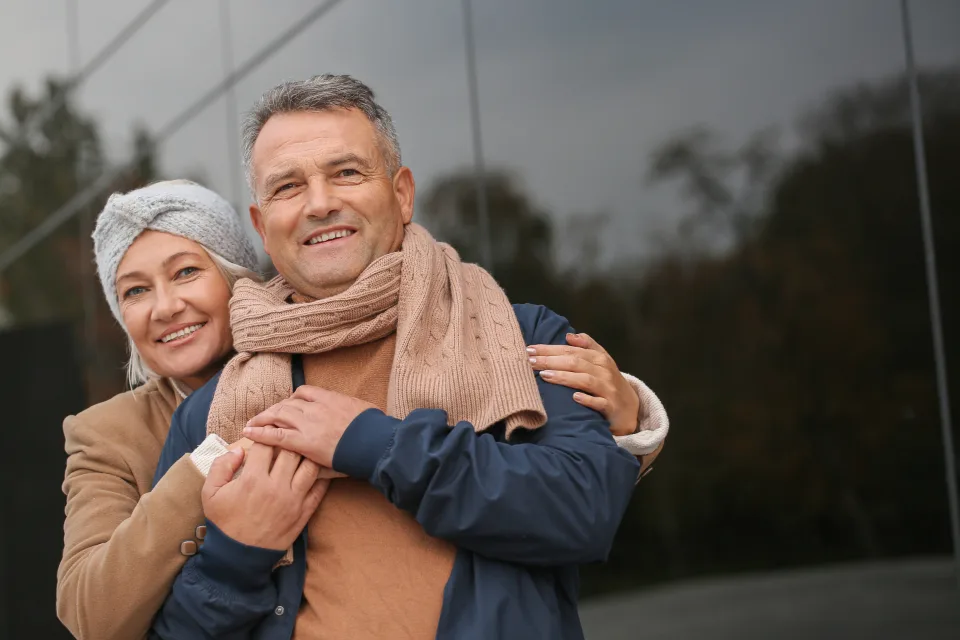 A smiling older couple in fall coats and scarves embracing outdoors
