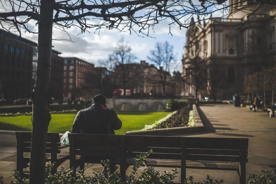 A person seen from behind sitting alone on a park bench in a city square