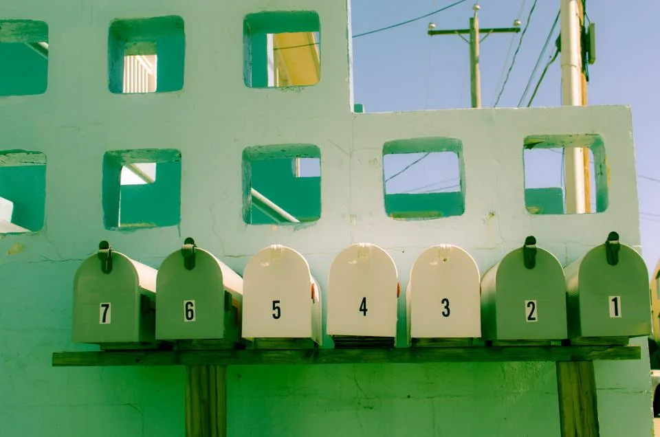 A row of numbered green mailboxes in front of a green wall