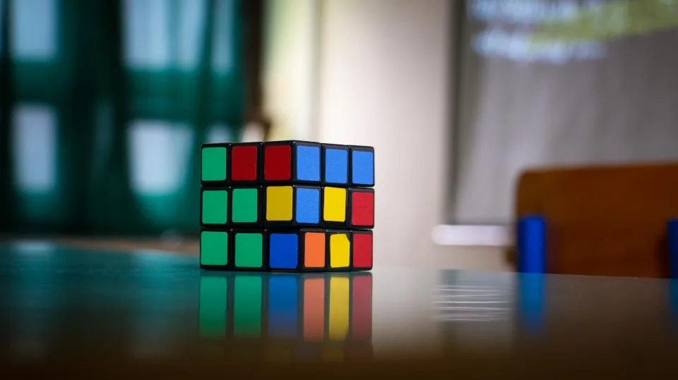 A scrambled puzzle cube sitting on a reflective table