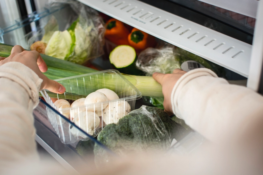 Hands placing fresh vegetables and mushrooms into a refrigerator drawer